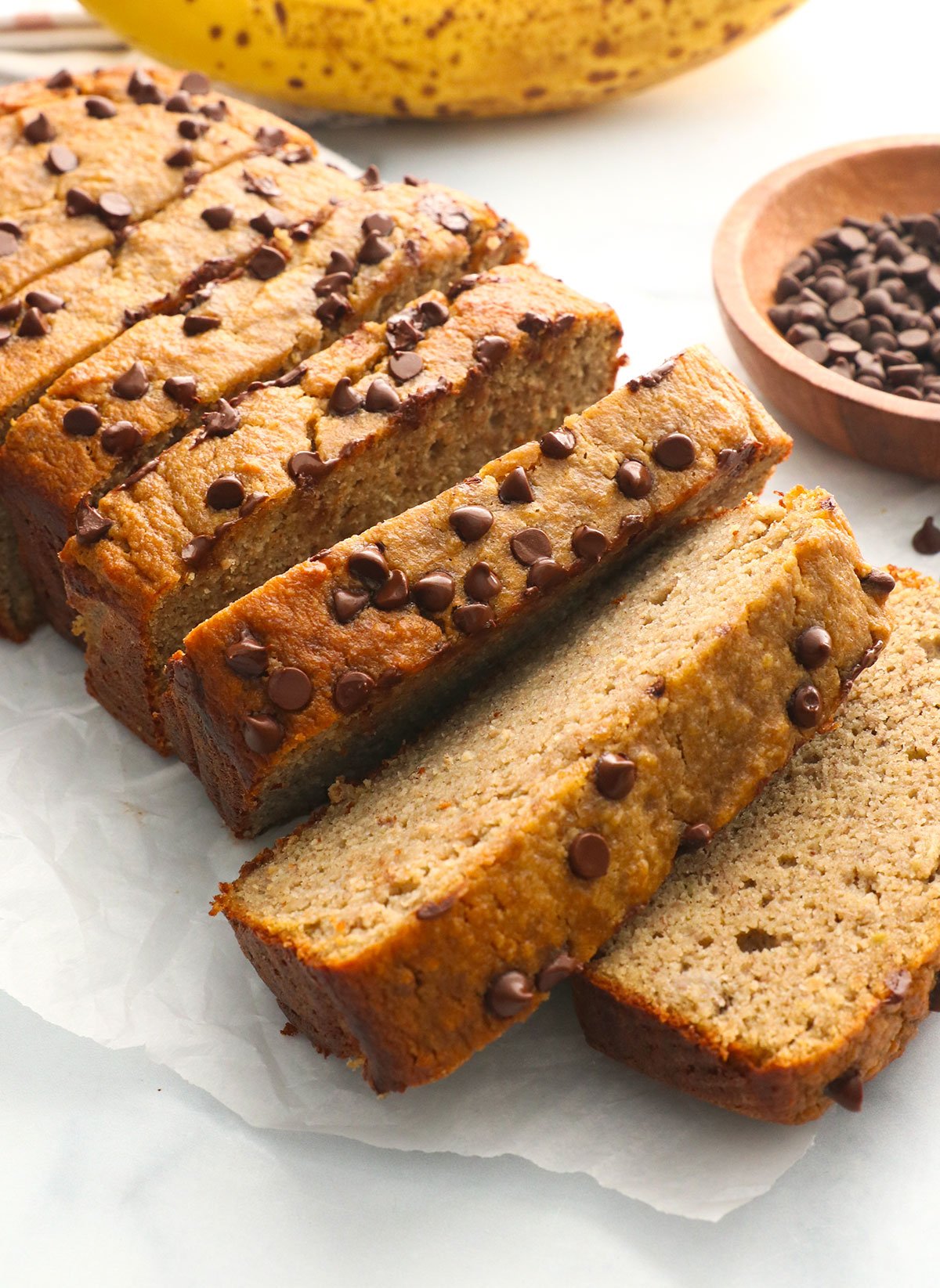 protein banana bread topped with chocolate chips and sliced on parchment paper.