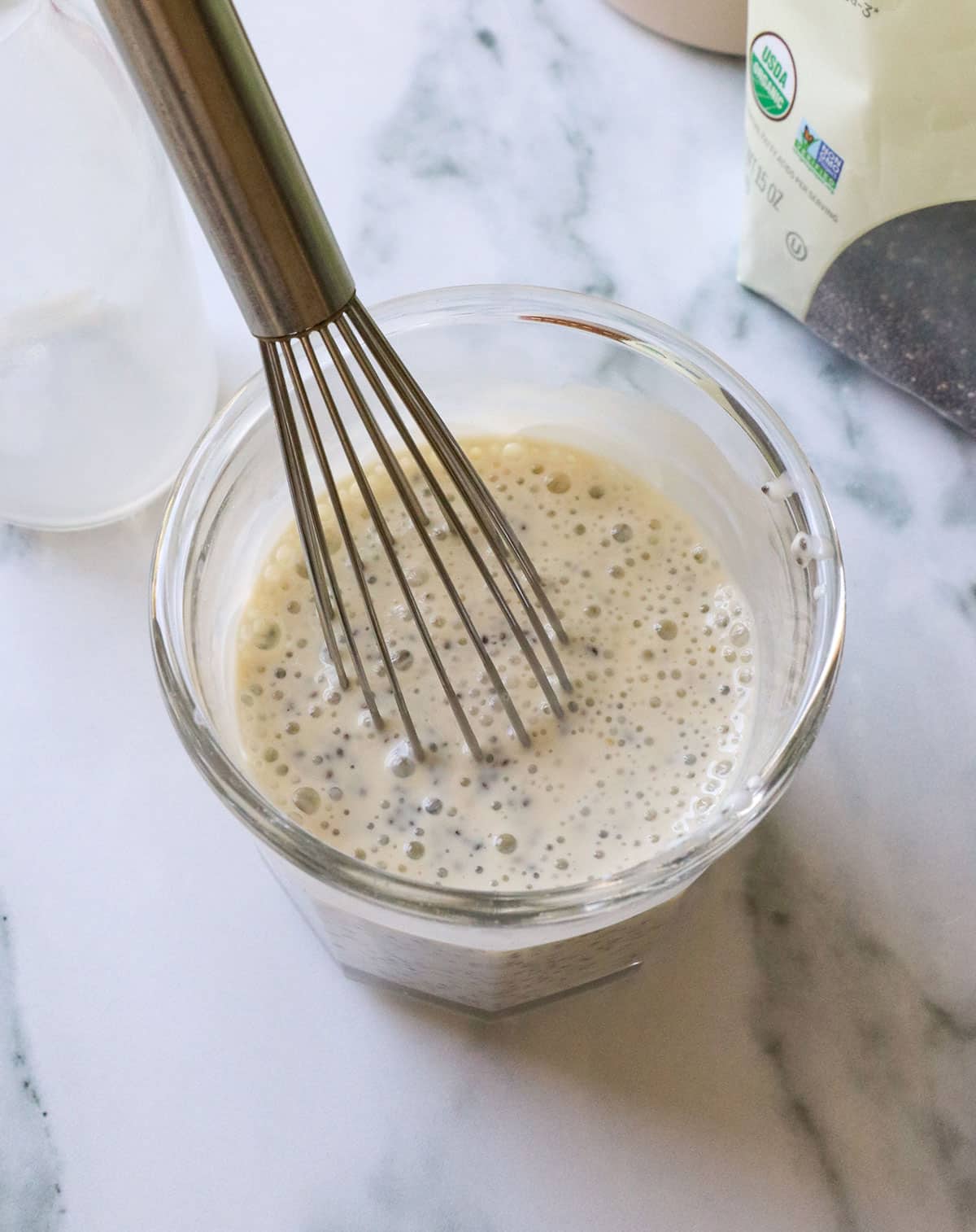 chia pudding stirred with a small whisk in a glass jar.