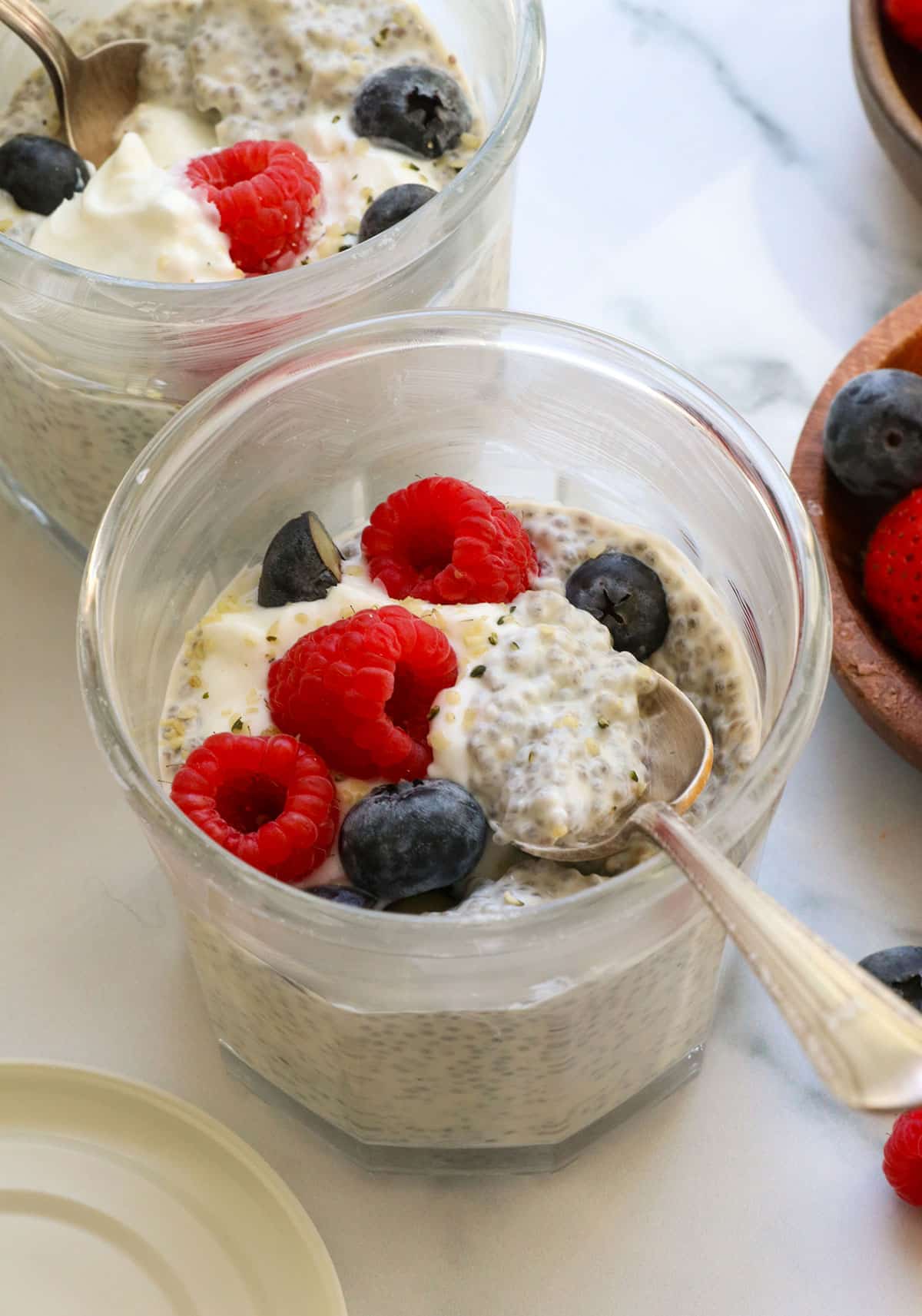 chia pudding with greek yogurt, berries, and hemp hearts on top served in a glass jar.