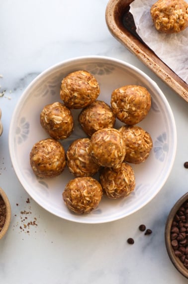 peanut butter protein balls in a white bowl with seeds on the side.