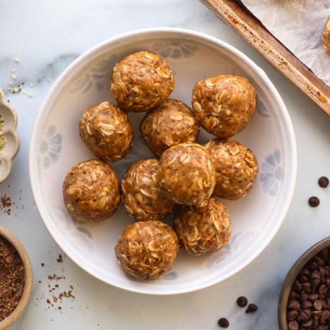 peanut butter protein balls in a white bowl with seeds on the side.