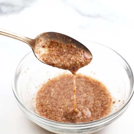 flax egg dripping off of a spoon into a glass bowl.