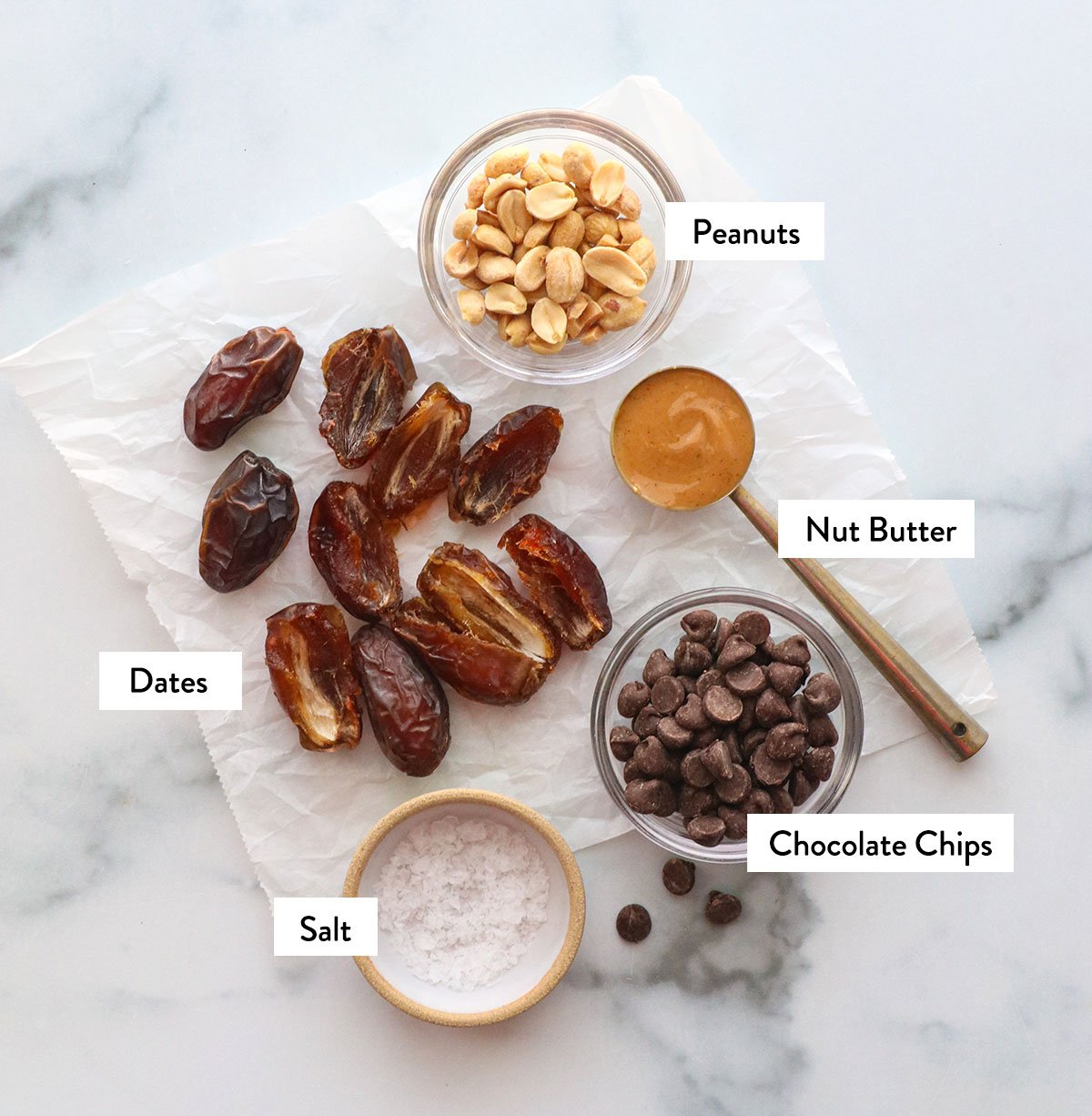 dates, peanuts, peanut butter and chocolate chips labeled on parchment paper.