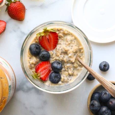 protein overnight oats in a glass jar with a lid nearby and berries.