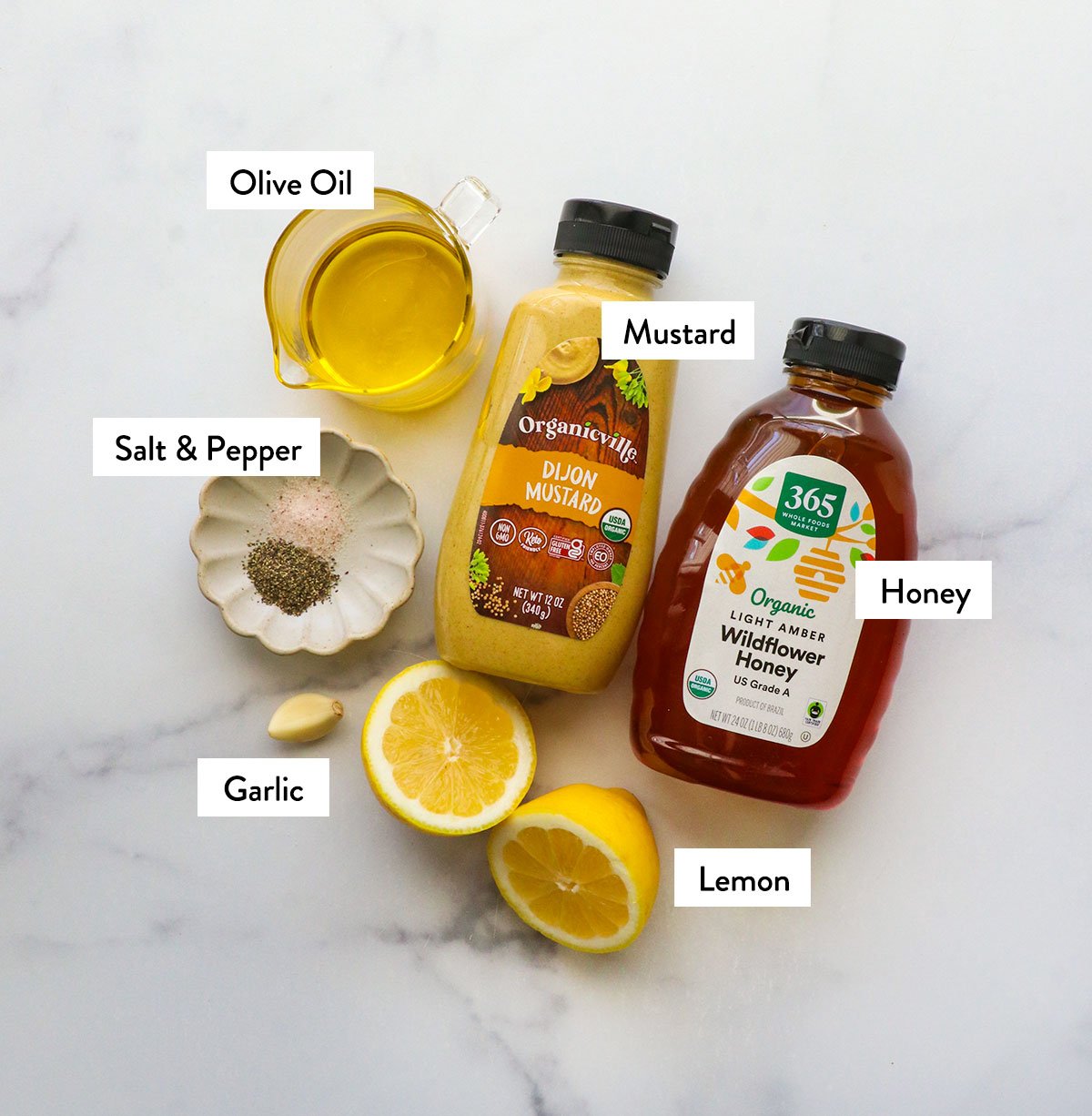 Mustard, honey, lemon, olive oil and spices marked on a white surface.