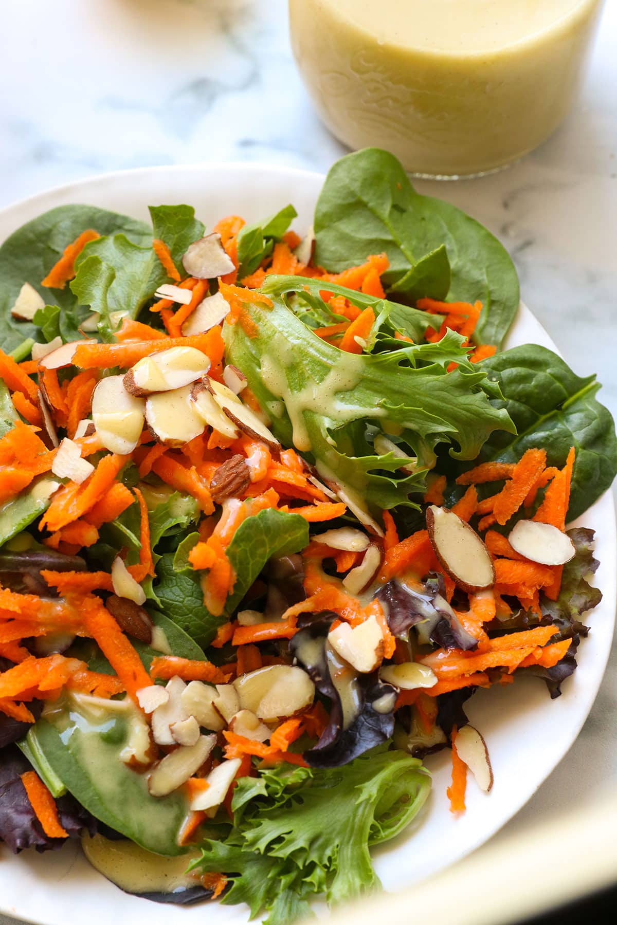 apple cider vinegar dressing drizzled on a leafy green salad with sliced almonds. 