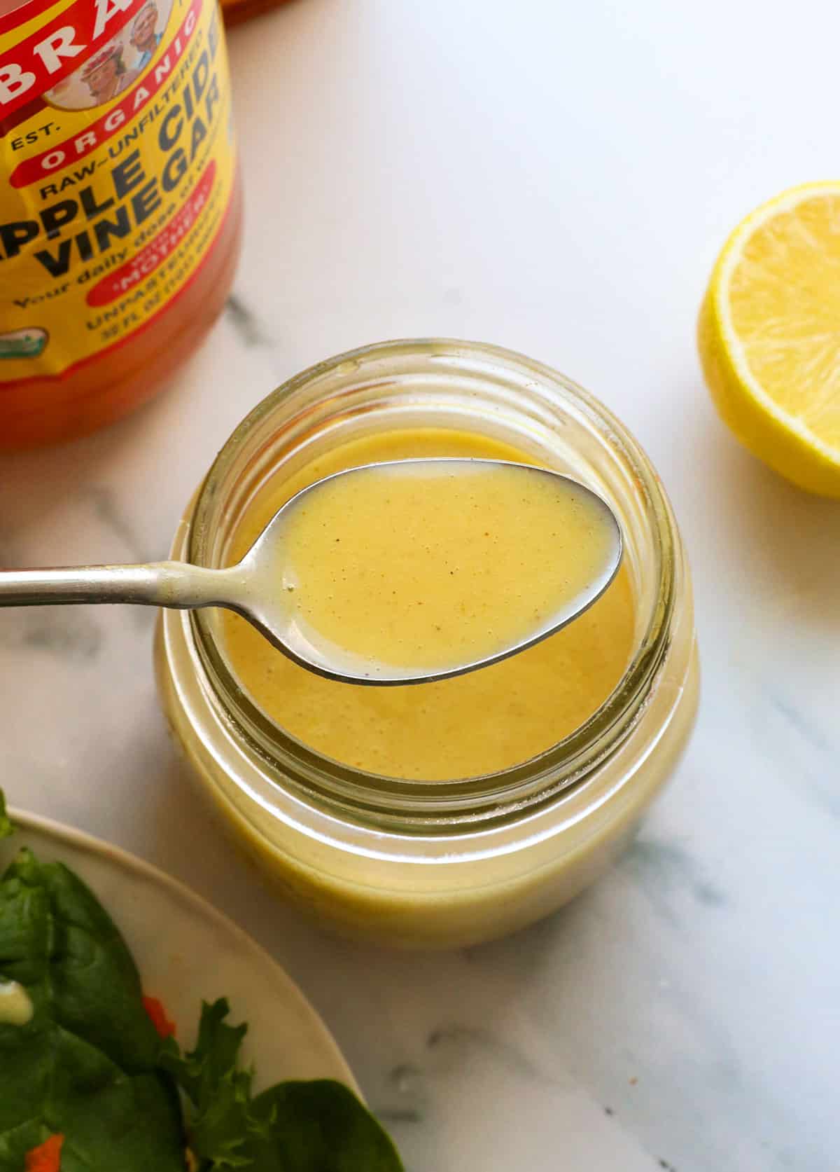 apple cider vinegar dressing lifted up on a spoon from the jar. 