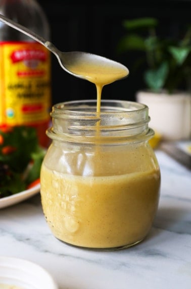 apple cider vinegar dressing dripping off of a spoon into the jar.