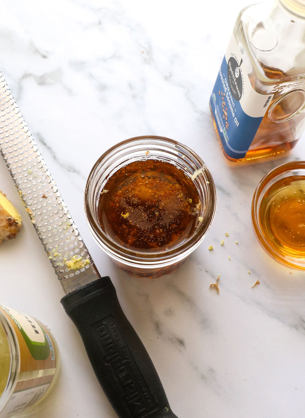 salad dressing ingredients added to a glass jar near a microplane.