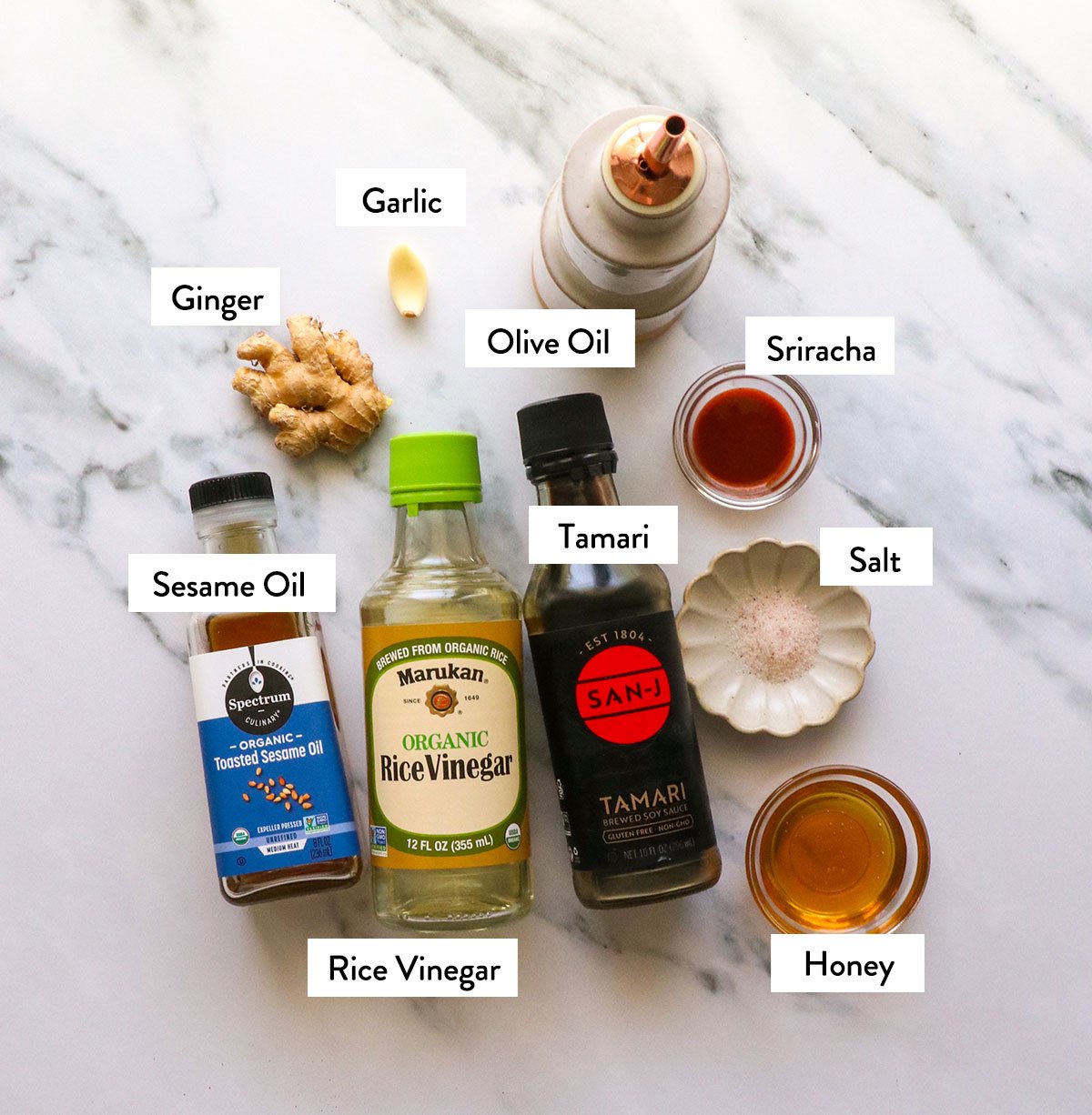 bottles of sesame oil, vinegar, tamari, honey, and spices labeled on a white surface.