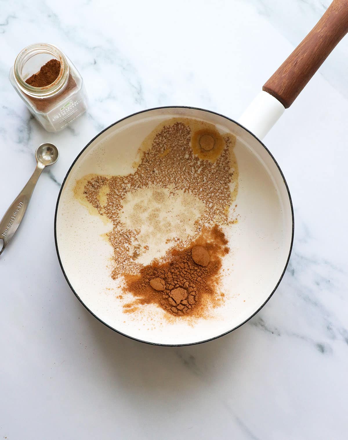 ground spices and milk added to a white saucepan.