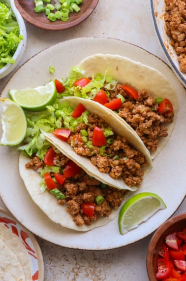 three turkey tacos on a plate with lettuce and tomatoes.