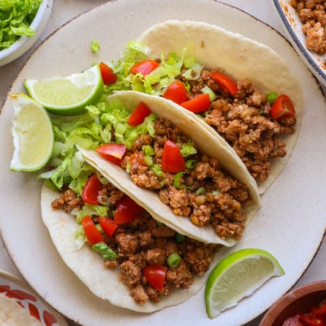 three turkey tacos on a plate with lettuce and tomatoes.