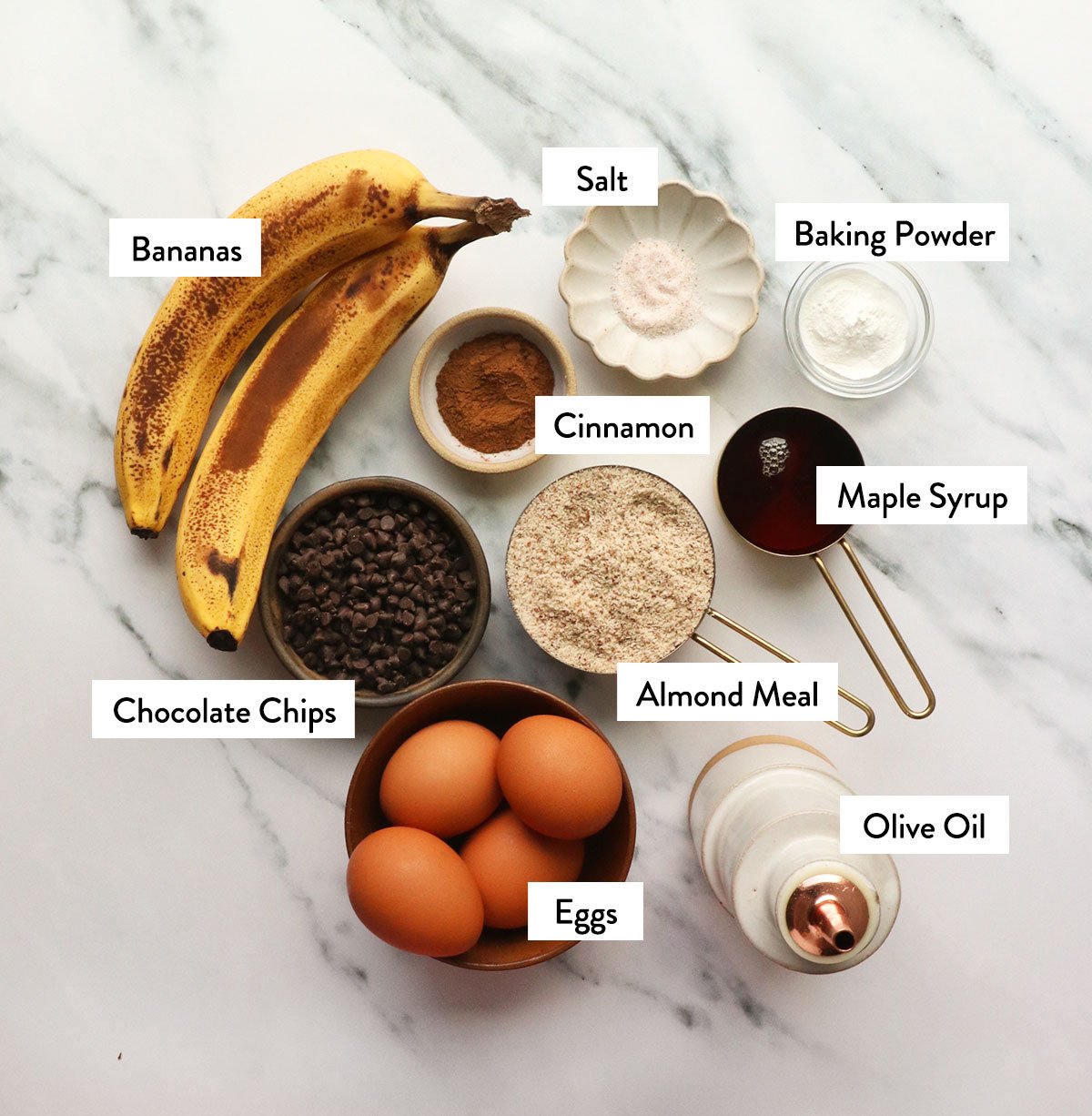 almond meal, bananas, maple syrup, eggs, and spices labeled in measuring cups. 