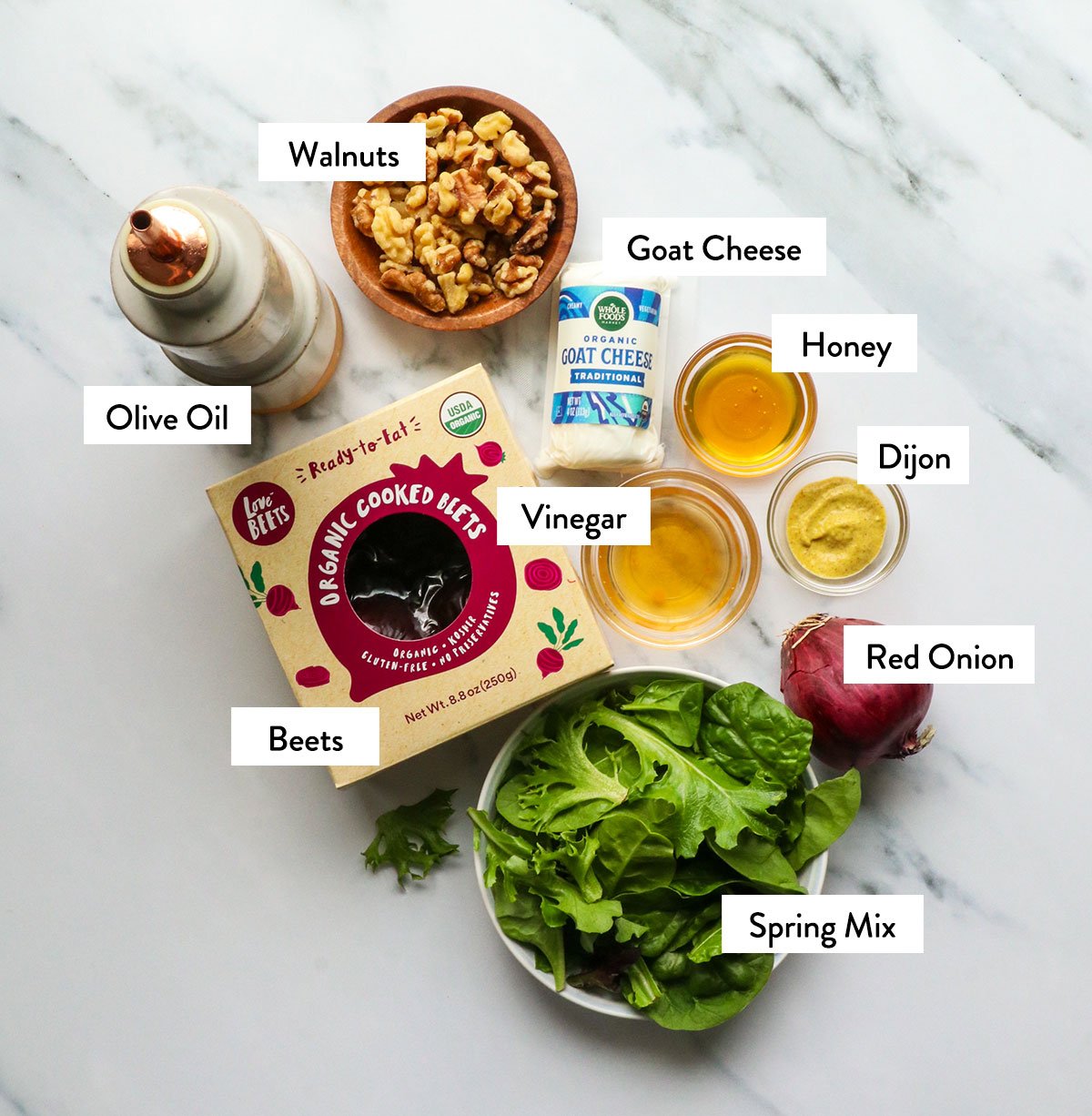 packaged beets, spring mix, walnuts, onion, and dressing ingredients labeled on a white surface. 