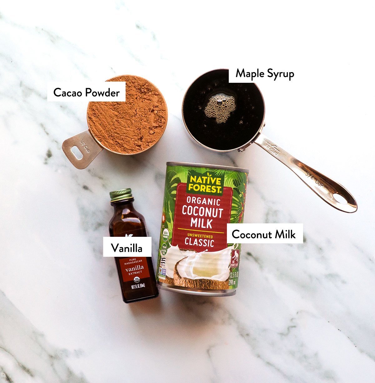 coconut milk, maple syrup, cacao powder, and vanilla extract labeled on a white surface.