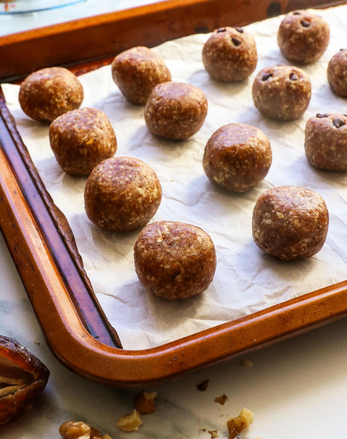 Several date energy balls on a parchment lined pan; some have chocolate chips pressed into the top.