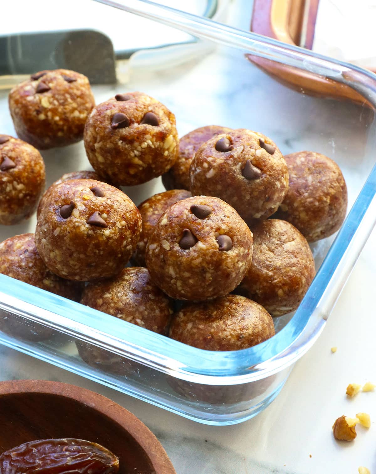date balls stored in a glass container with some chocolate chips pressed on top.