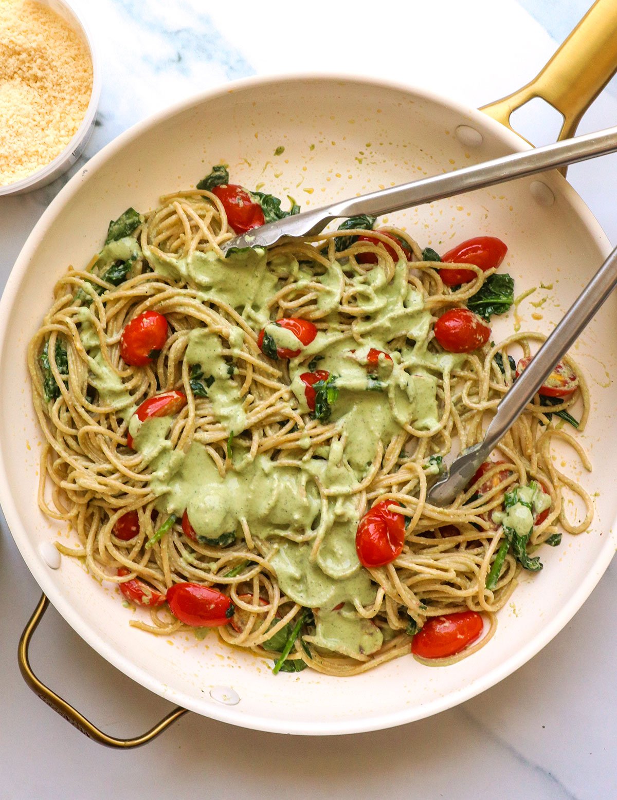 creamy pesto sauce in a skillet with cherry tomatoes and spinach. 