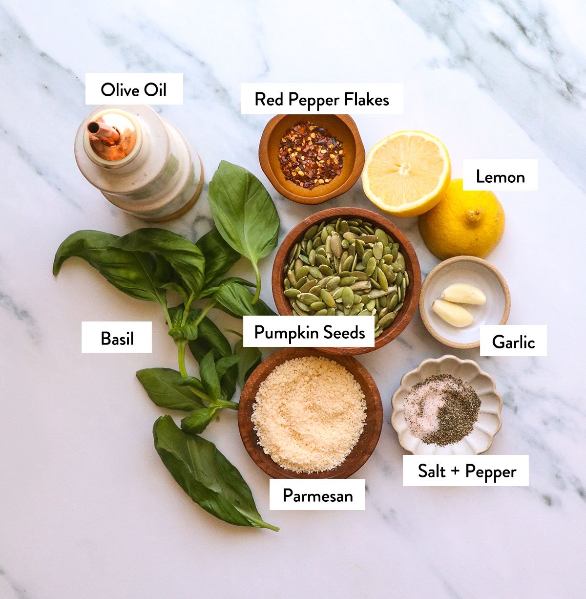 basil, parmesan, pumpkin seeds, lemon, and spices labeled on a white surface. 
