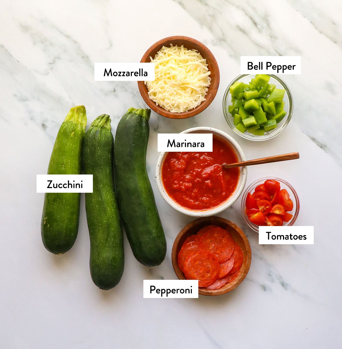 zucchini pizza boat ingredients labeled on a marble surface. 