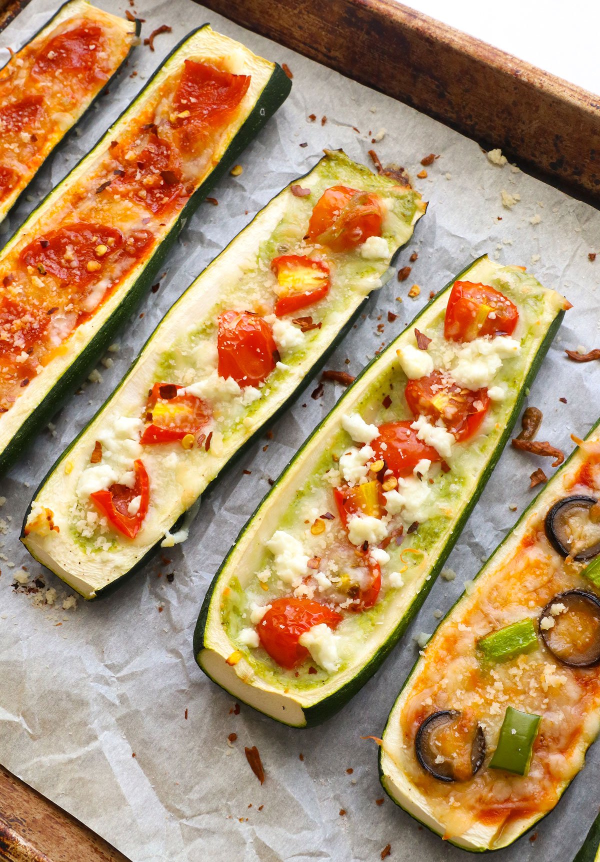 zucchini boats filled with pesto and tomatoes on a pan.