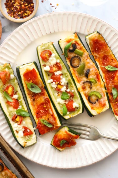 zucchini pizza boats with different toppings on a plate.