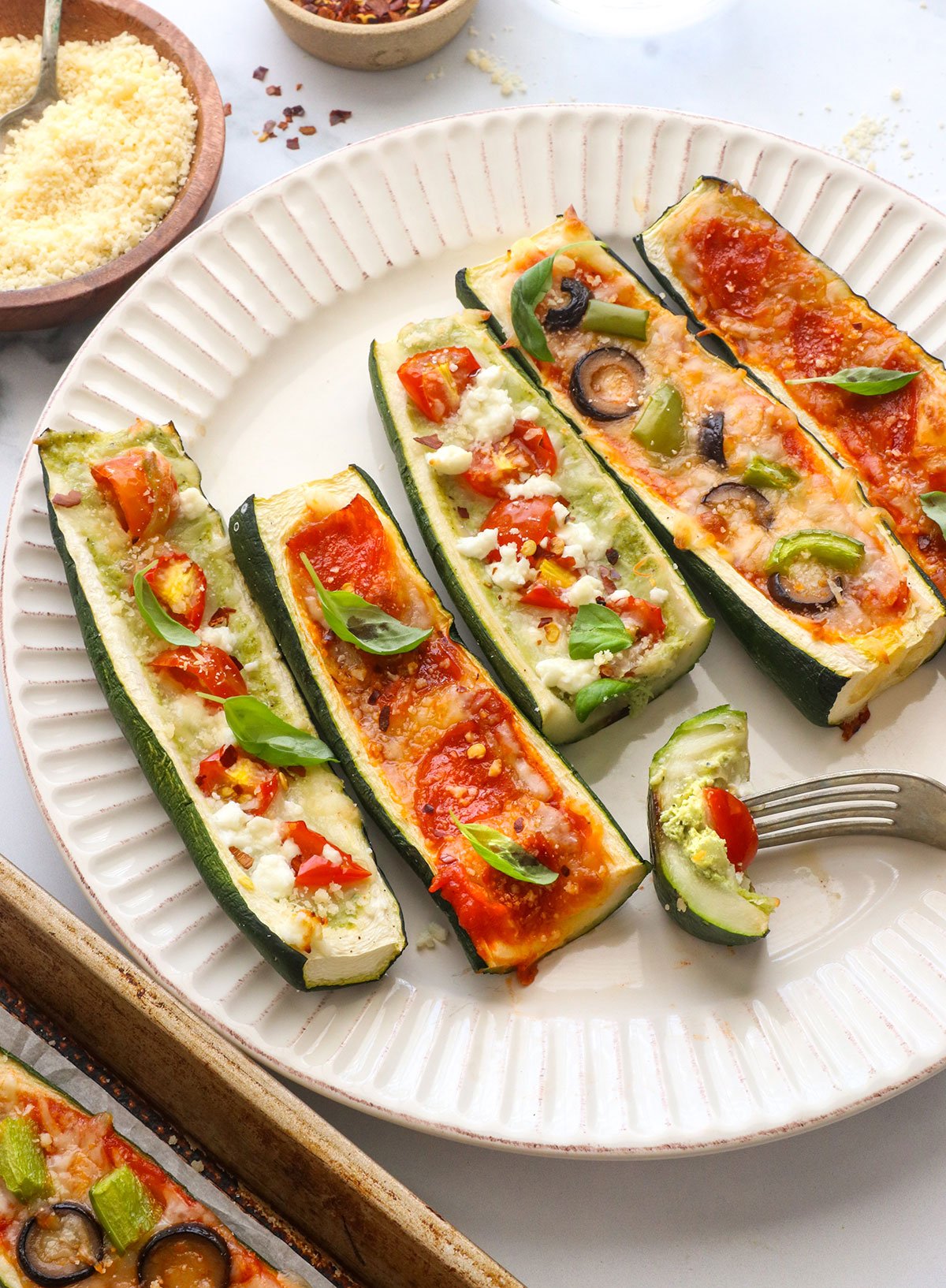 5 zucchini pizza boats served on a one plate with a fork taking a bite.