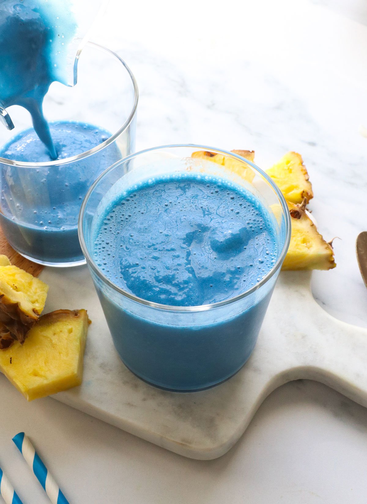 blue smoothie poured into two glasses on a white surface. 