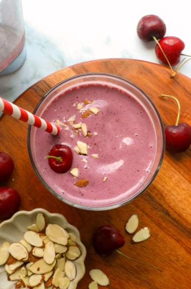 cherry smoothie on a wooden board with sliced almonds.