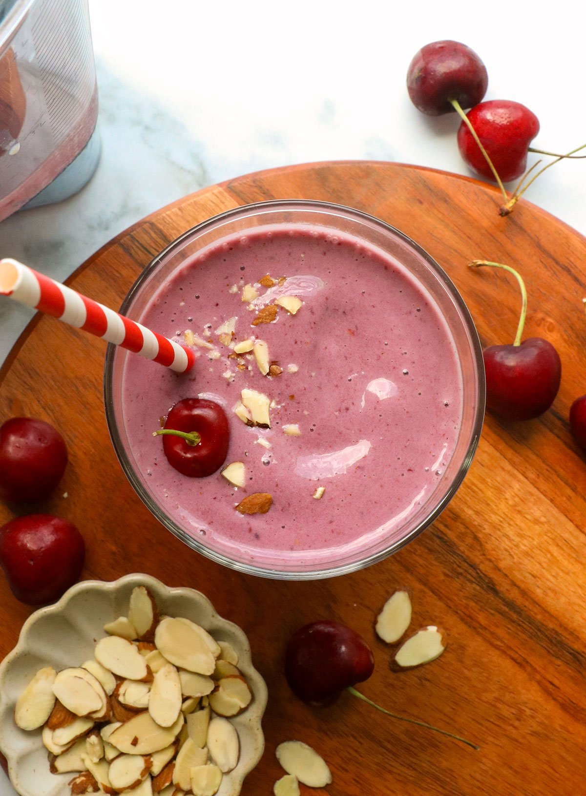 cherry smoothie on a wooden board with sliced almonds.