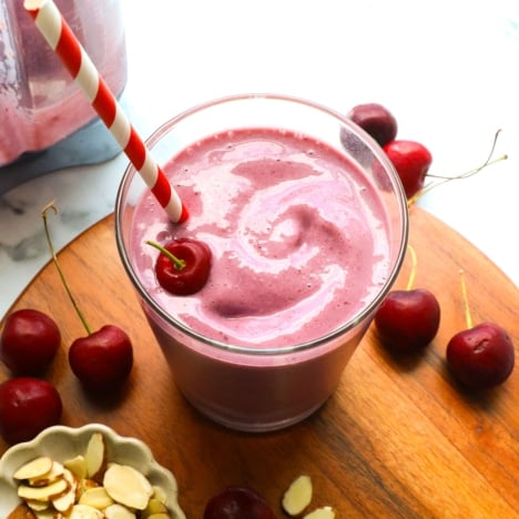 cherry smoothie in a glass near a bowl of almonds and cherries.