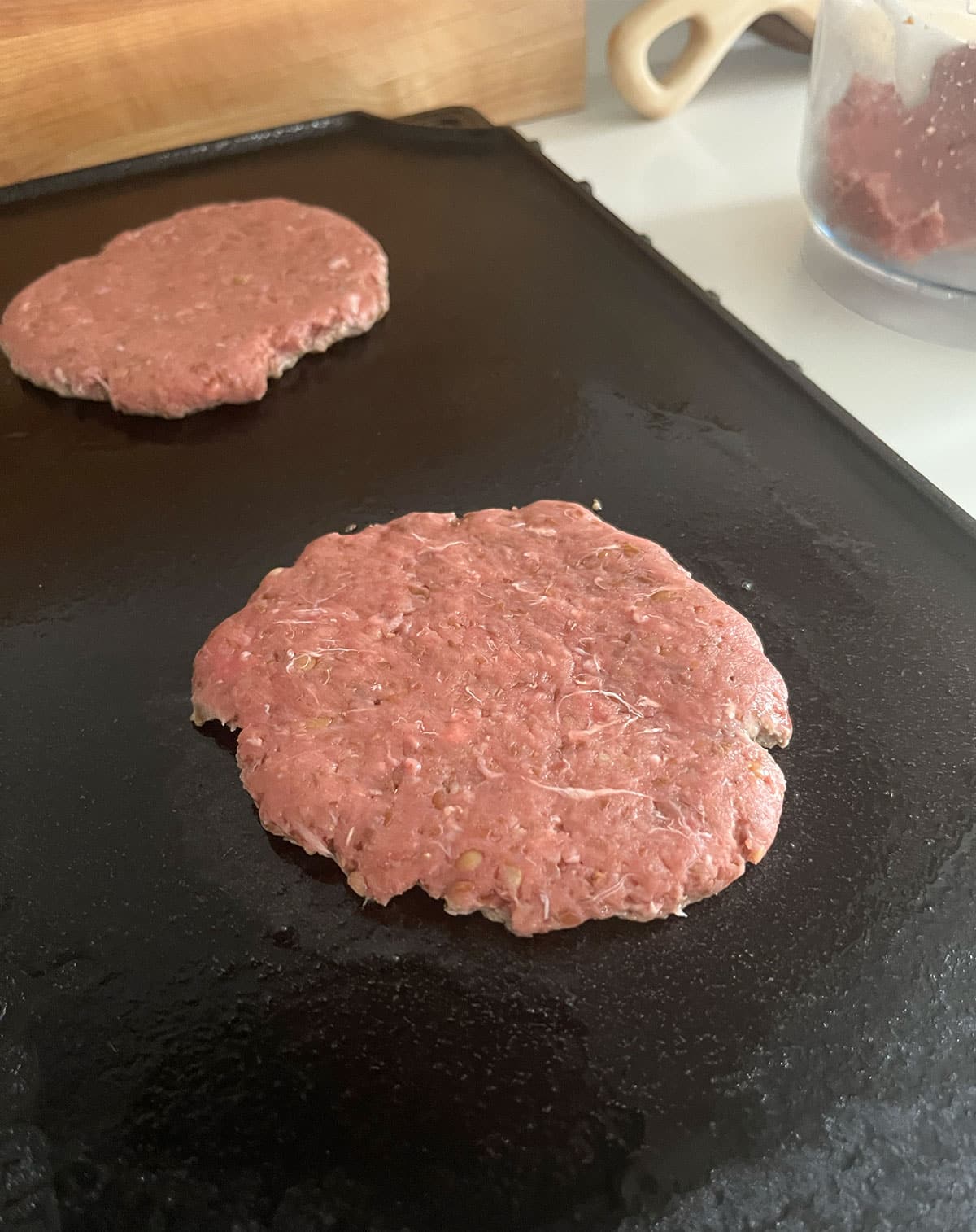 cast iron griddle cooking two burgers at the same time.