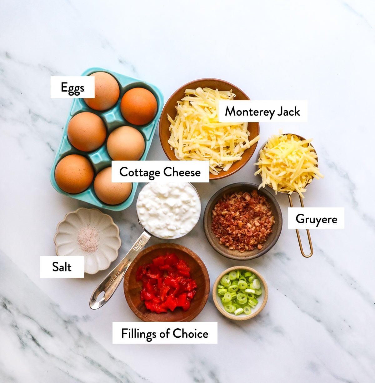 eggs, cottage cheese, shredded cheese, and toppings on a white surface. 