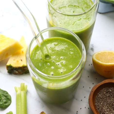 glowing green smoothie served in two glasses with a straw.