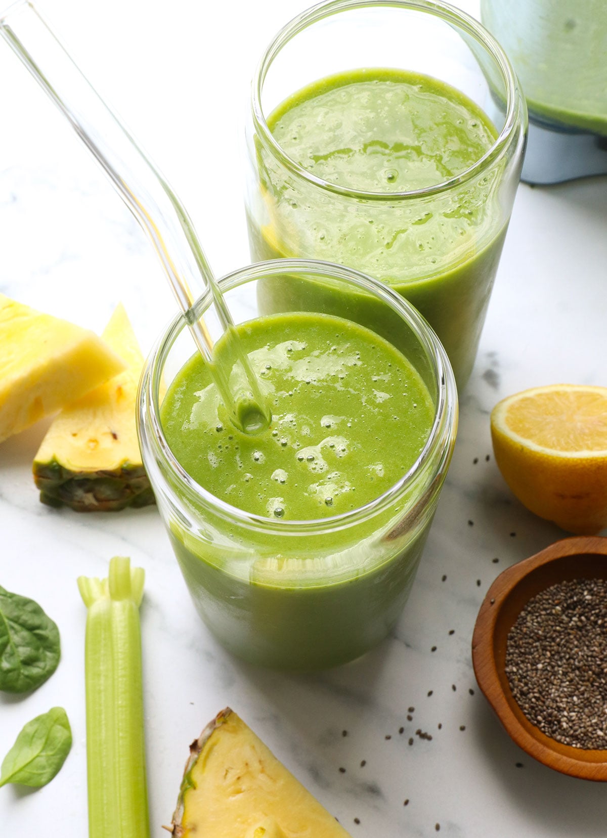 glowing green smoothie served in two glasses with a straw.