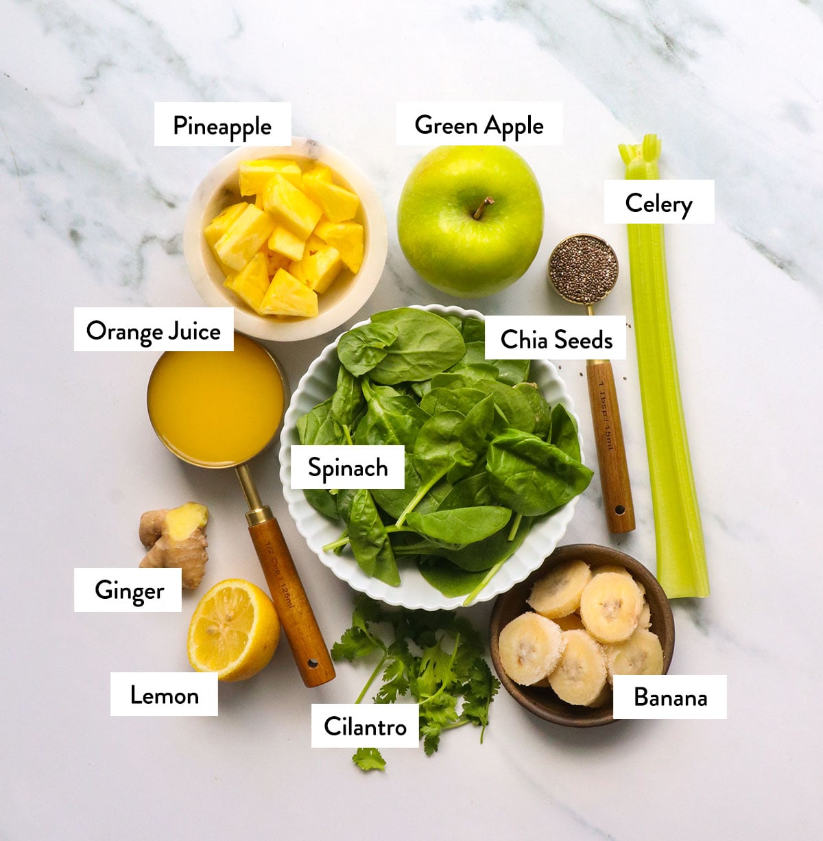 green apple, pineapple, spinach, celery, cilantro, chia seeds, and banana labeled on a white surface.