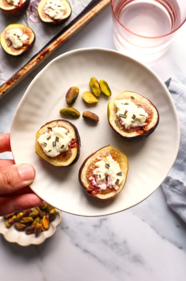 fig appetizer lifted on a small plate with a side of nuts.