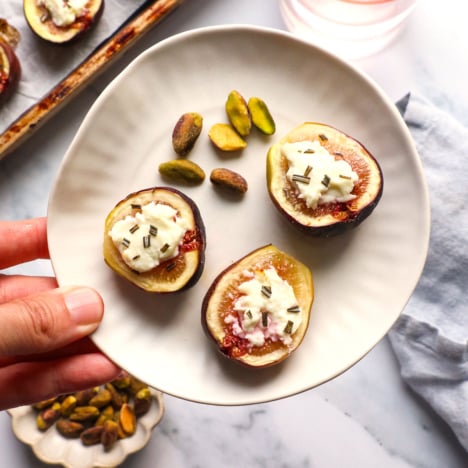 fig appetizer lifted on a small plate with a side of nuts.