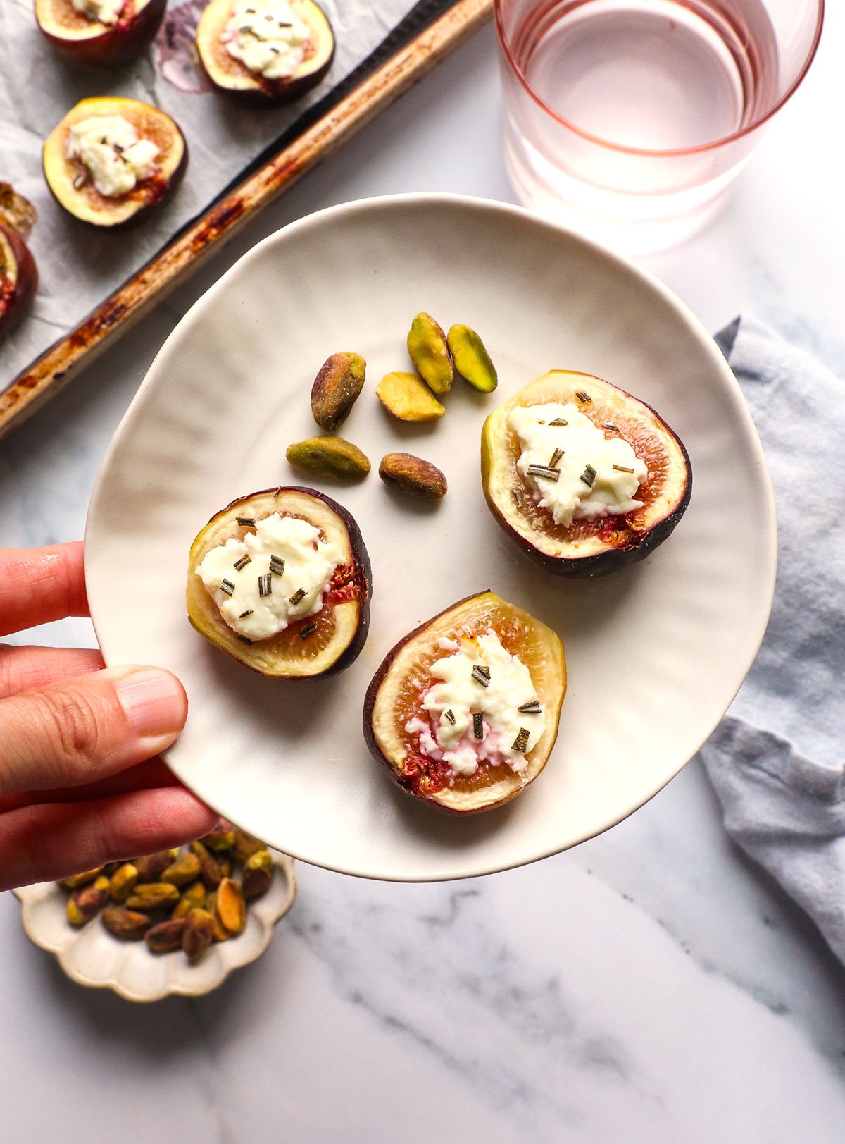 fig appetizer lifted on a small plate with a side of nuts. 