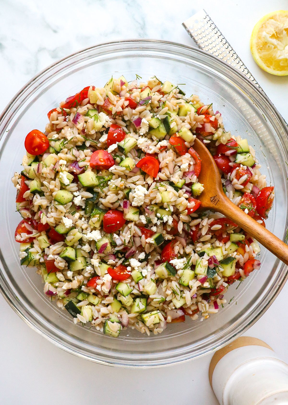 lemon orzo salad in a large glass bowl with a wooden spoon. 
