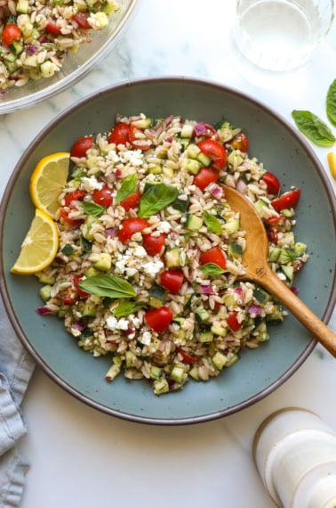 lemon orzo salad served in a blue bowl with lemon slices.