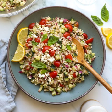lemon orzo salad served in a blue bowl with lemon slices.