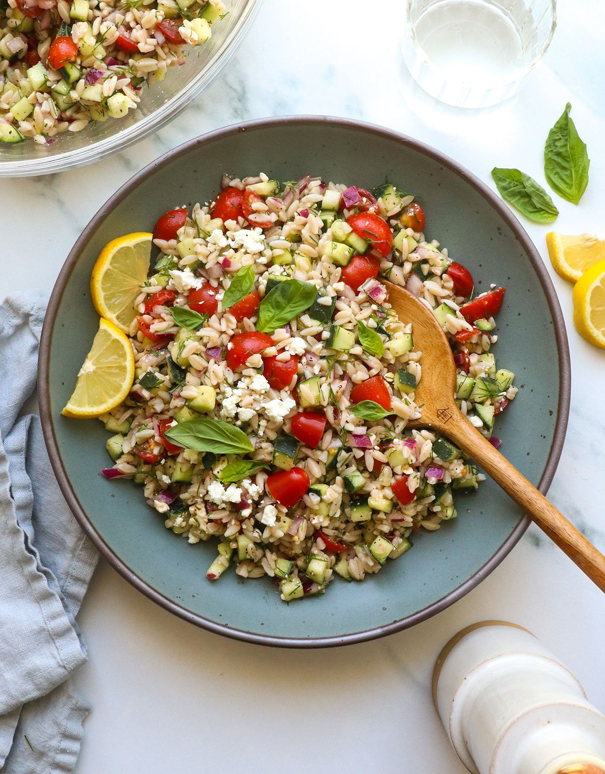 lemon orzo salad served in a blue bowl with lemon slices.  