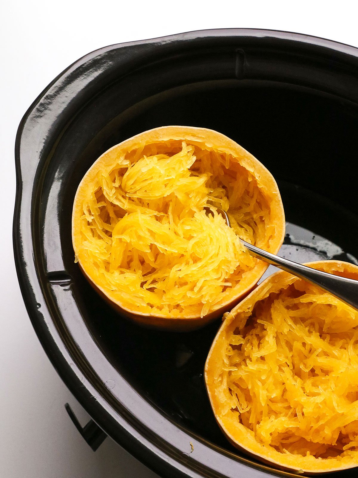 spaghetti squash half in a slow cooker with strands scooped with a fork. 