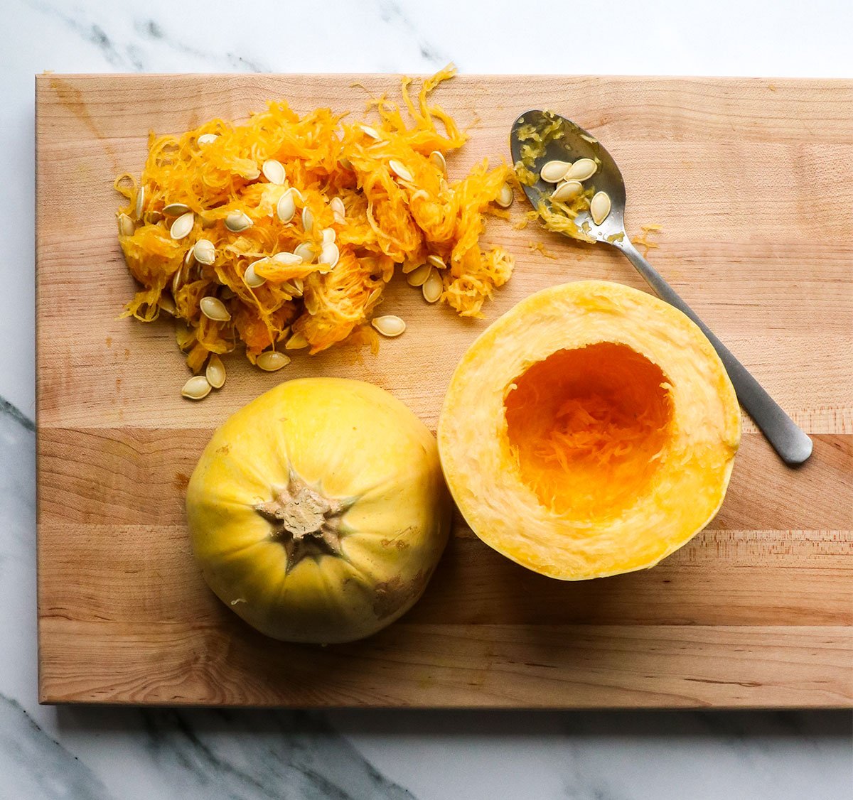 spaghetti squash cut in half crosswise with seeds scooped out on cutting board. 