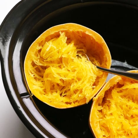 spaghetti squash cooked in a black slow cooker with a fork.