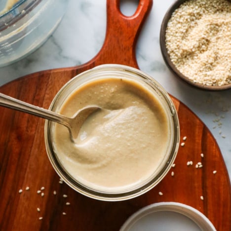 homemade tahini stirred with a spoon in a glass jar.