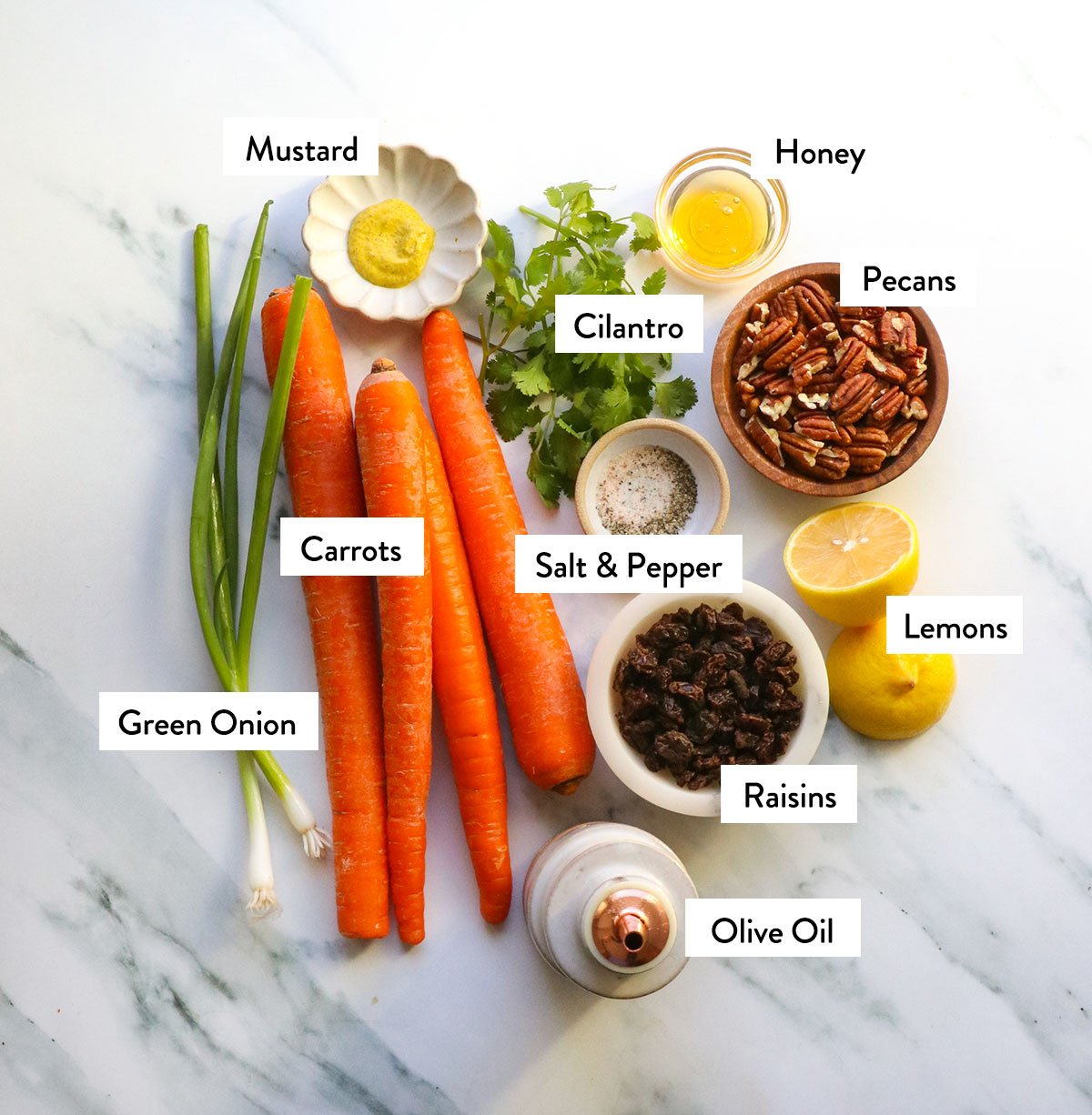 carrots, green onion, cilantro, pecans, raisins and lemon juice labeled in bowls. 