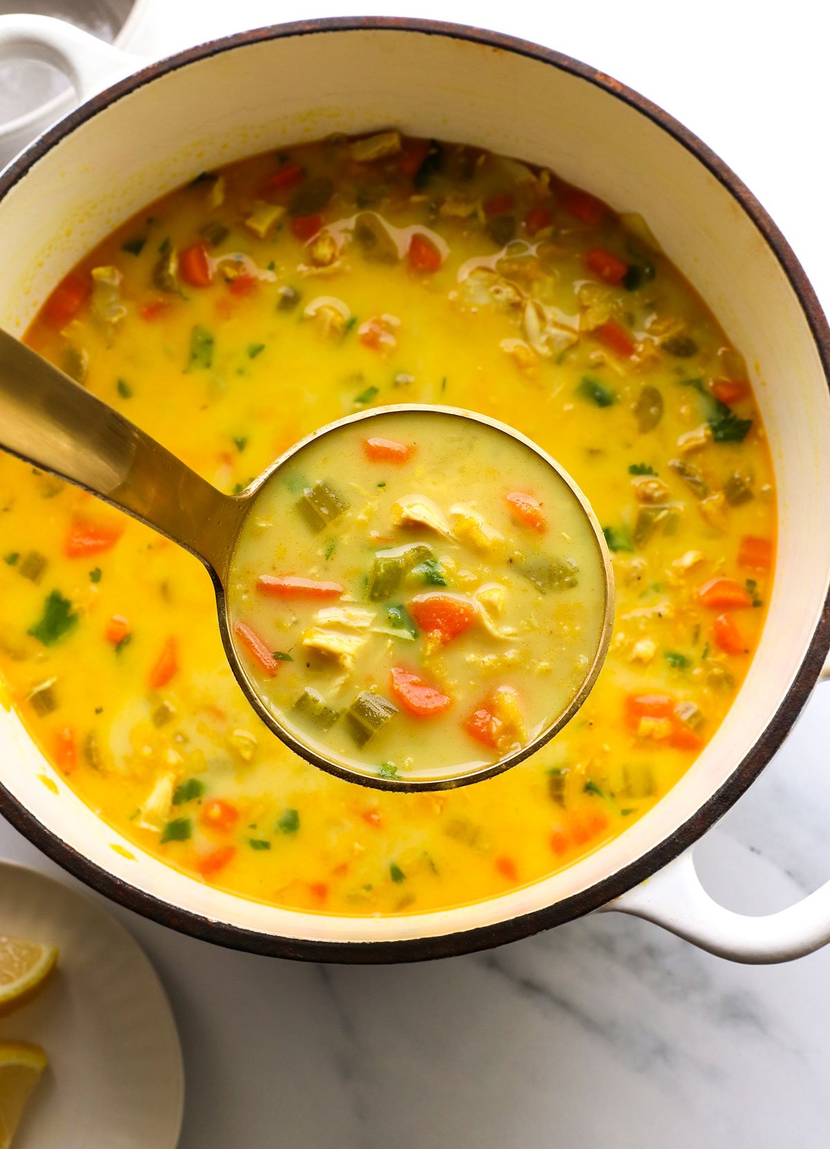 ladle of curry soup with chicken over a white pot. 